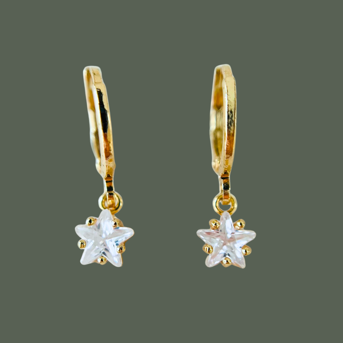 Gold earrings with star-shaped clear stones on a gray background