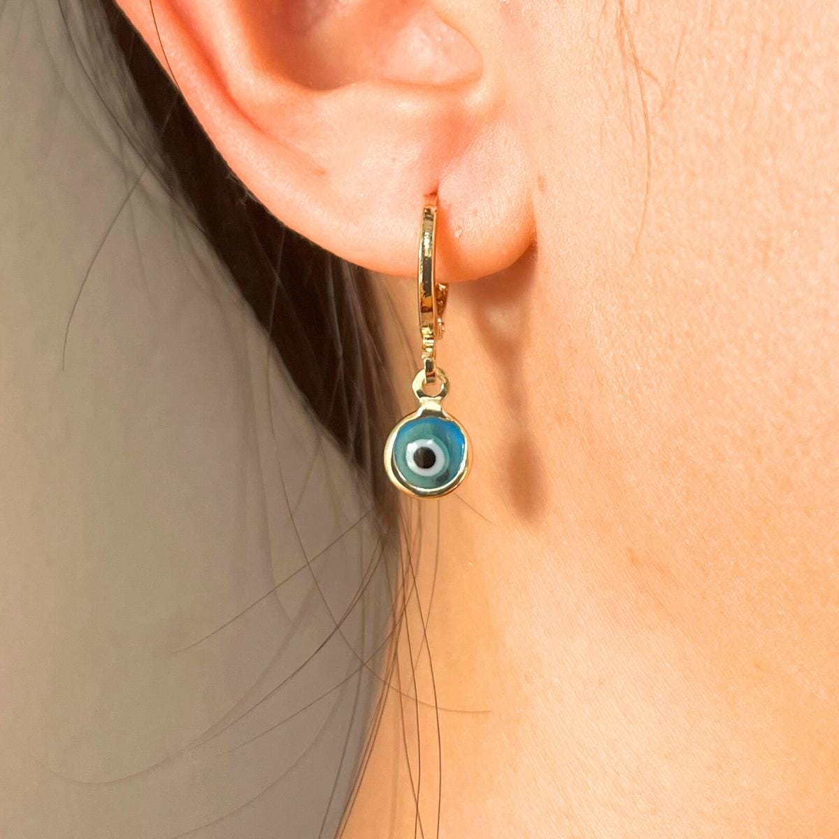 Gold plated hoop earring with a glass blue evil eye charm worn by a person.