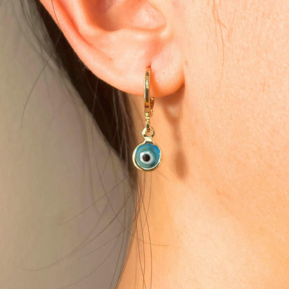 Gold plated hoop earring with a glass blue evil eye charm worn by a person.