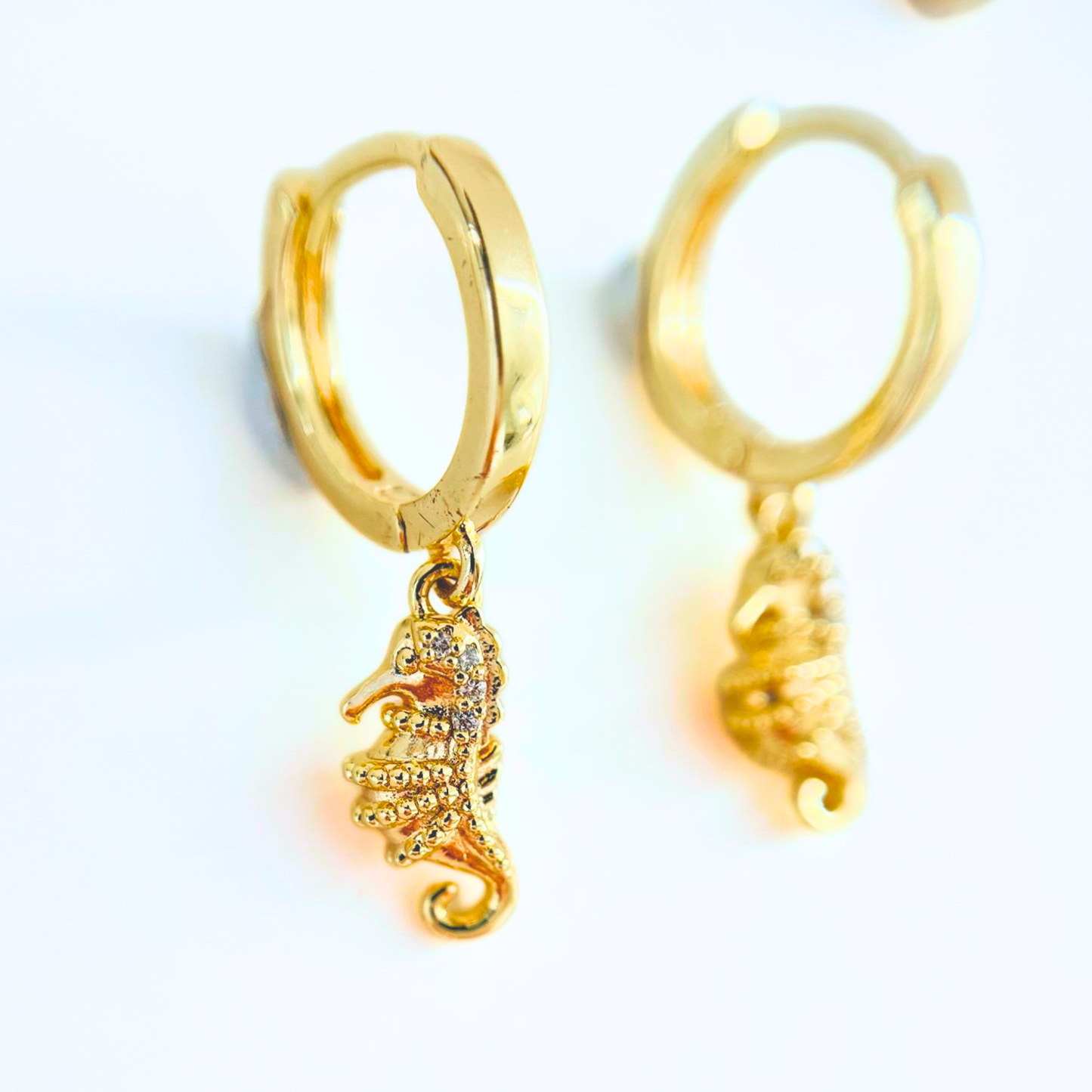 Gold hoop earrings with seahorse charms on a white background