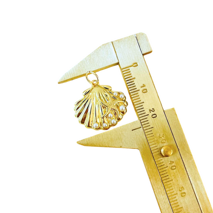 Gold scallop shell pendant with pearls on a gold caliper against a white background