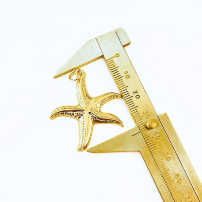 Gold starfish pendant being measured with a gold caliper on a white background