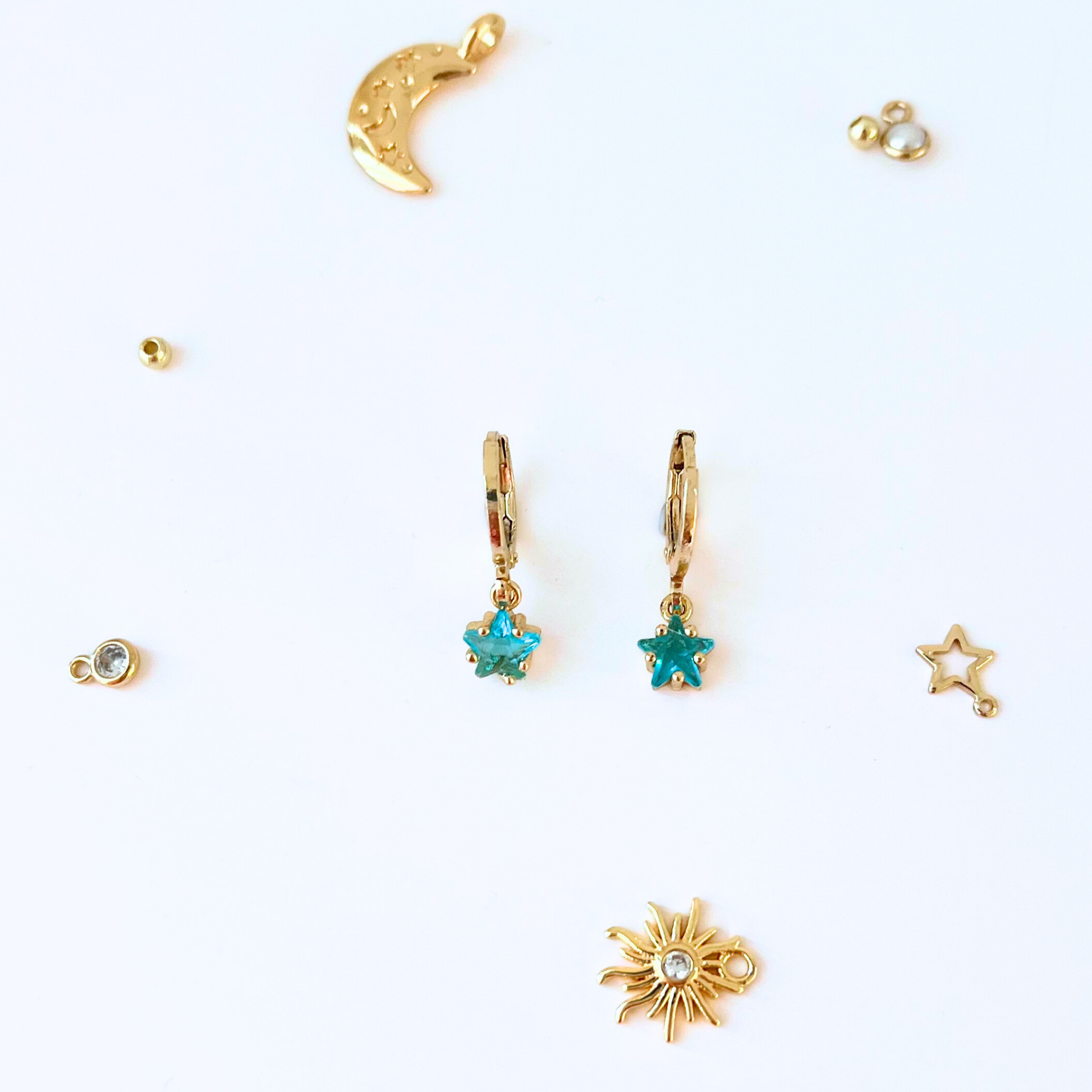 Collection of gold jewelry charms including a moon, star, and sun on a white background
