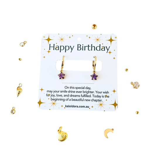 Gold earrings with star and shell charms on a 'Happy Birthday' card with decorative elements.