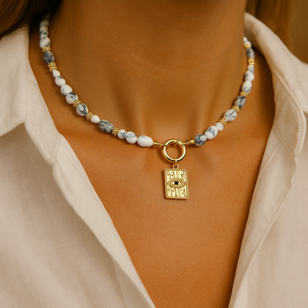 Natural Howlite Gemstone Necklace with a gold evil eye Rectangle pendant on a person wearing a beige shirt.