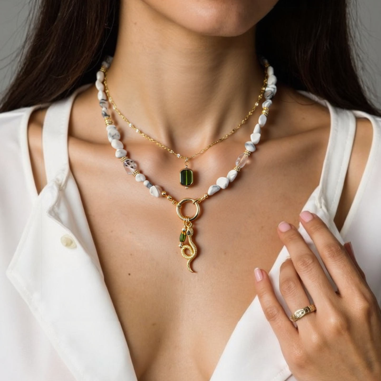 Close-up of a woman wearing a Green CZ Eyes Gold Plated Snake Pendant and natural howlite gemstone necklace, against a neutral background.