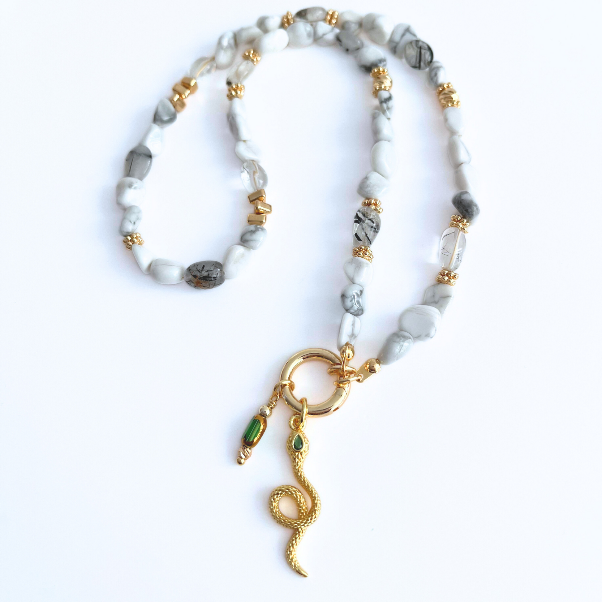 natural howlite gemstone Necklace with Green CZ Eyes Gold Plated Snake Pendant and green glass bead charm on a white background