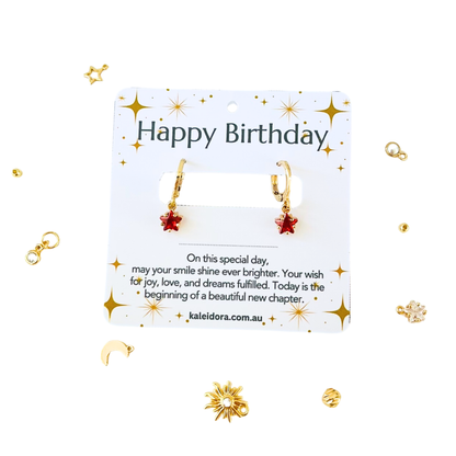 Gold earrings on a 'Happy Birthday' card with decorative elements on a white background