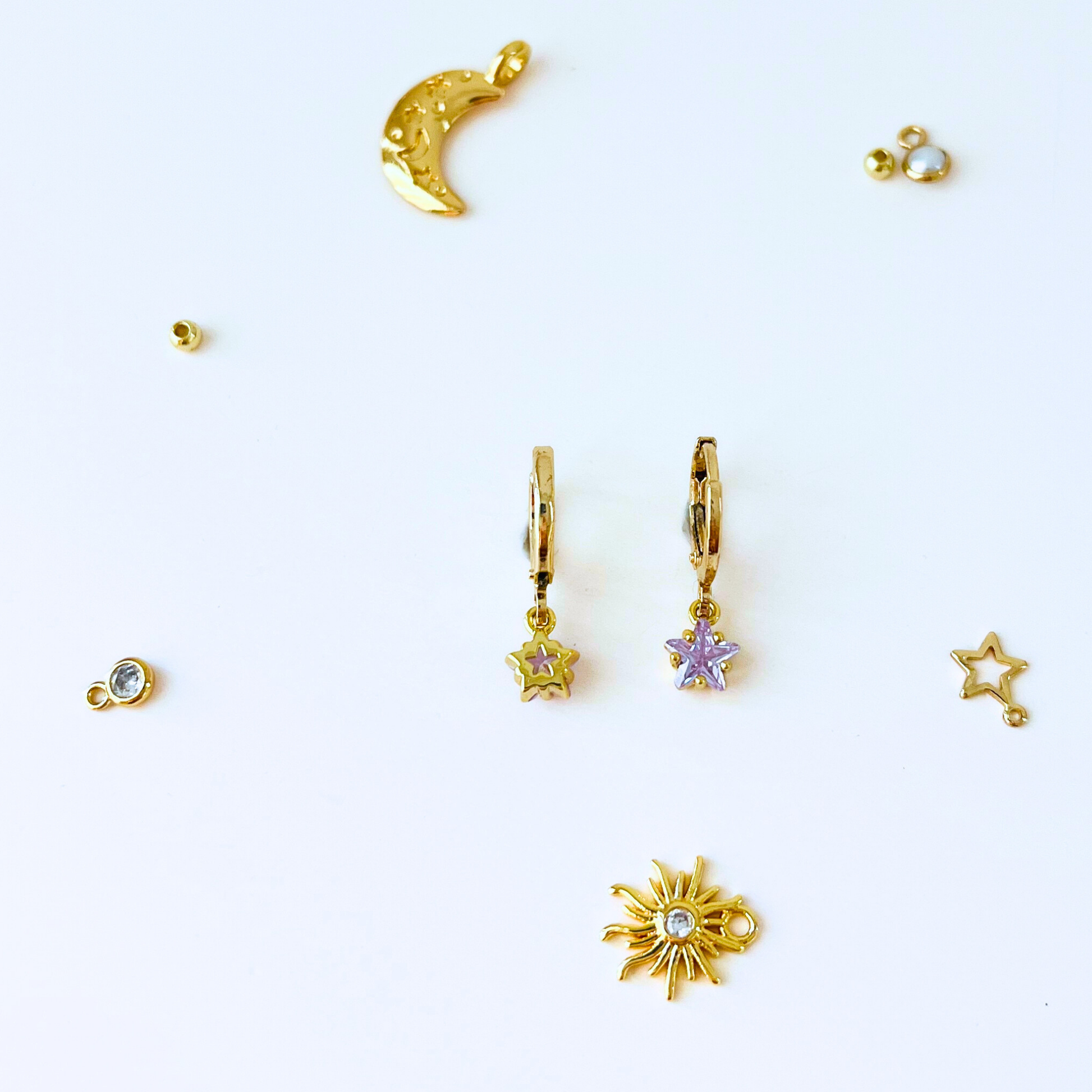 Gold jewelry charms including a moon, star, and sun on a white background