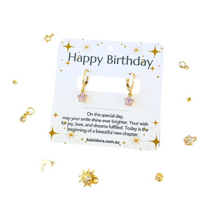 Gold earrings on a 'Happy Birthday' card with decorative elements on a white background
