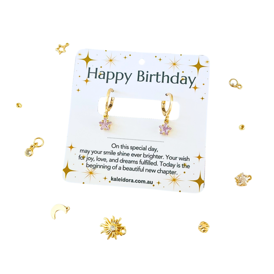 Gold earrings on a 'Happy Birthday' card with decorative elements on a white background