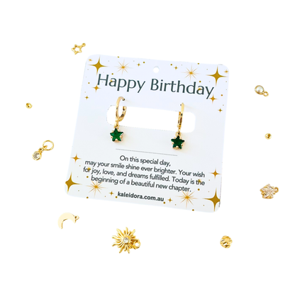 Gold earrings on a 'Happy Birthday' card with decorative elements on a white background