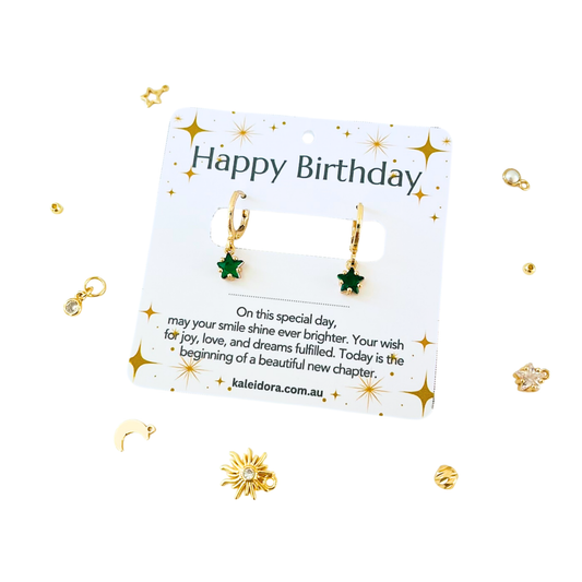 Gold earrings on a 'Happy Birthday' card with decorative elements on a white background
