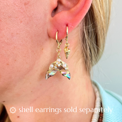Close-up of a person wearing stack earrings a mermaid tail earrings and a shell earrings with a blurred background.