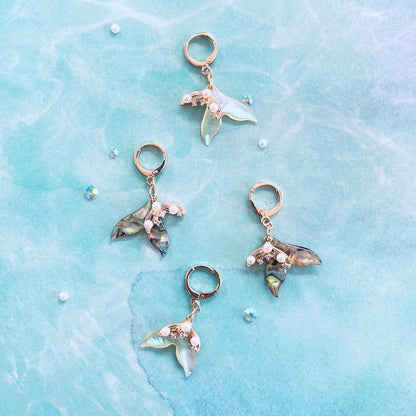 A pair of abalone earrings with a pair of white shell earrings on a light blue water textured background