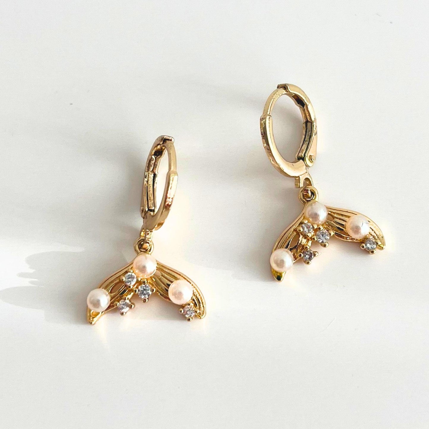 Gold plated mermaid tail hoop earrings with pearl and CZ accents on a white background