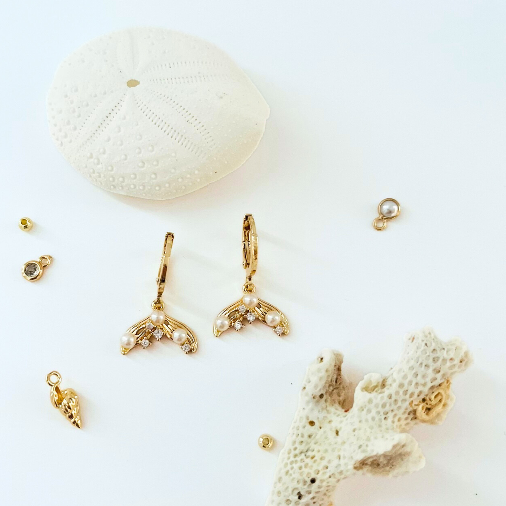 Gold plated mermaid tail earrings with CZ and pearls on a white background with coral and shell decorations