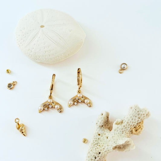 Gold plated mermaid tail earrings with CZ and pearls on a white background with coral and shell decorations