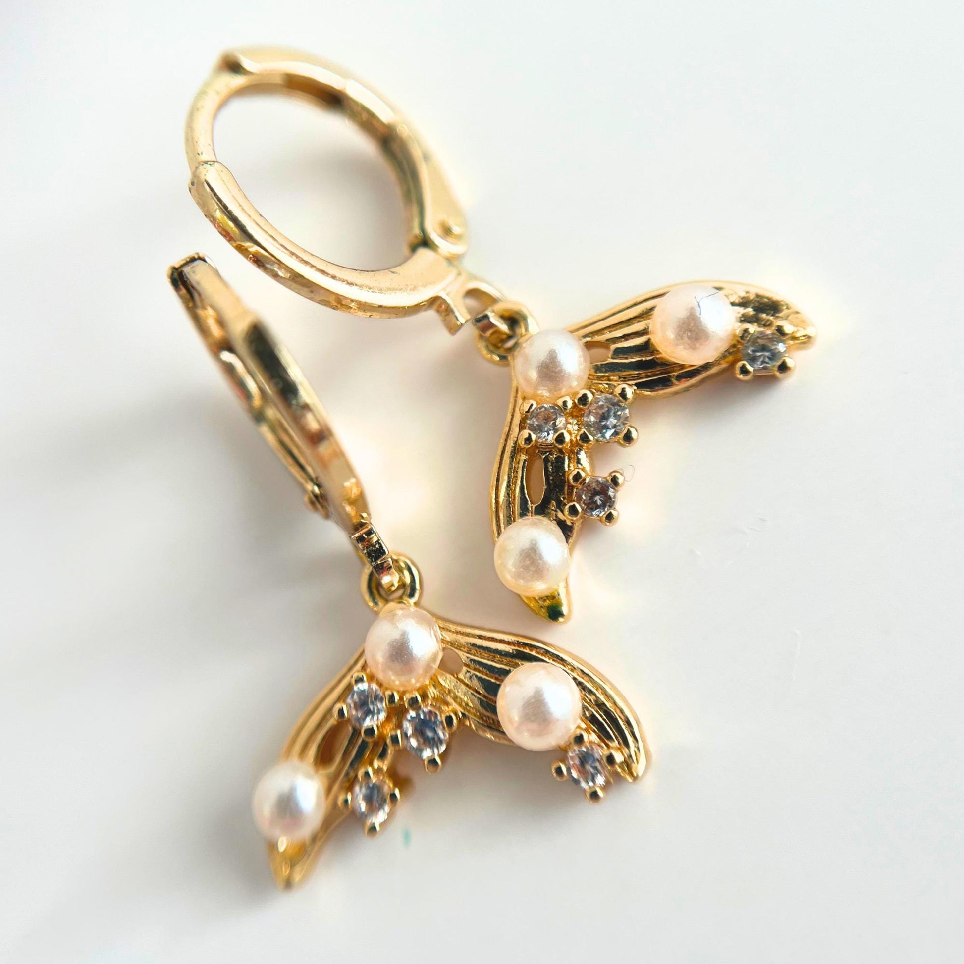 Gold mermaid tail earrings with pearls and rhinestones on a white background