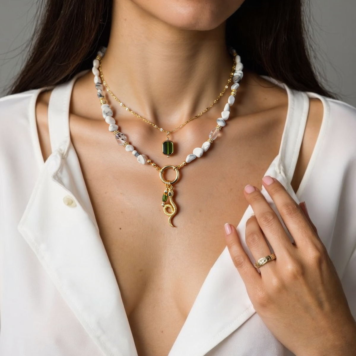 Woman wearing a gold necklace with a green pendant and a white top.